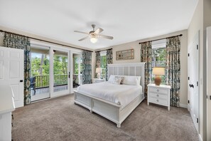 Une chambre dotée d’un grand lit, d’un ventilateur de plafond, d’une table de chevet, d’une lampe et offrant une vue sur l’extérieur grâce à une porte-fenêtre coulissante.