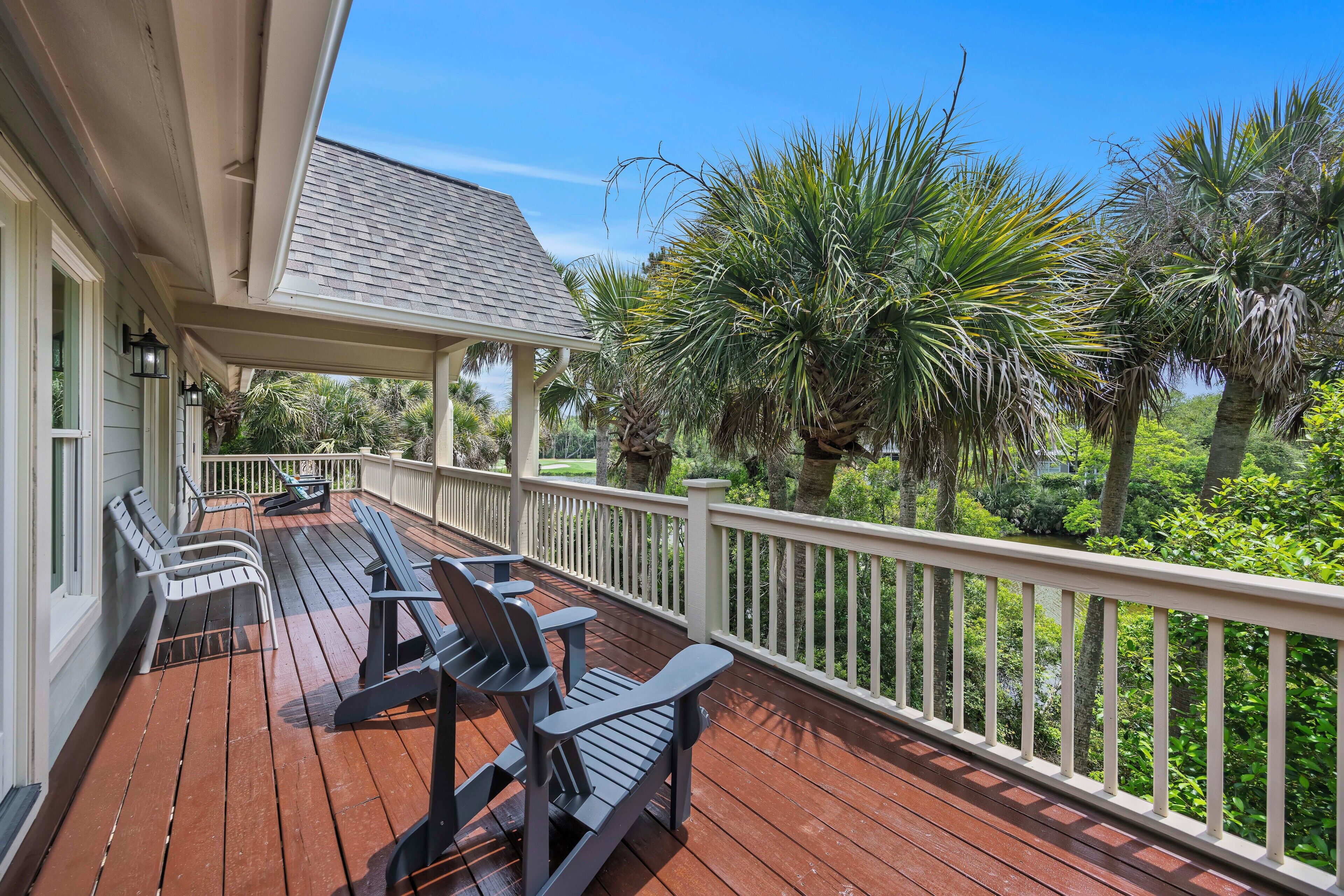 A covered deck with outdoor seating, surrounded by lush greenery and palm trees.