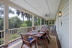 Une véranda abritée, avec une table à manger pour quatre personnes, entourée de chaises en bois dotées de coussins bleus.