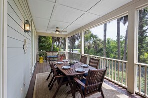Une terrasse couverte avec une table à manger pour quatre personnes, entourée de chaises, et offrant une vue sur de grands arbres et une rambarde.