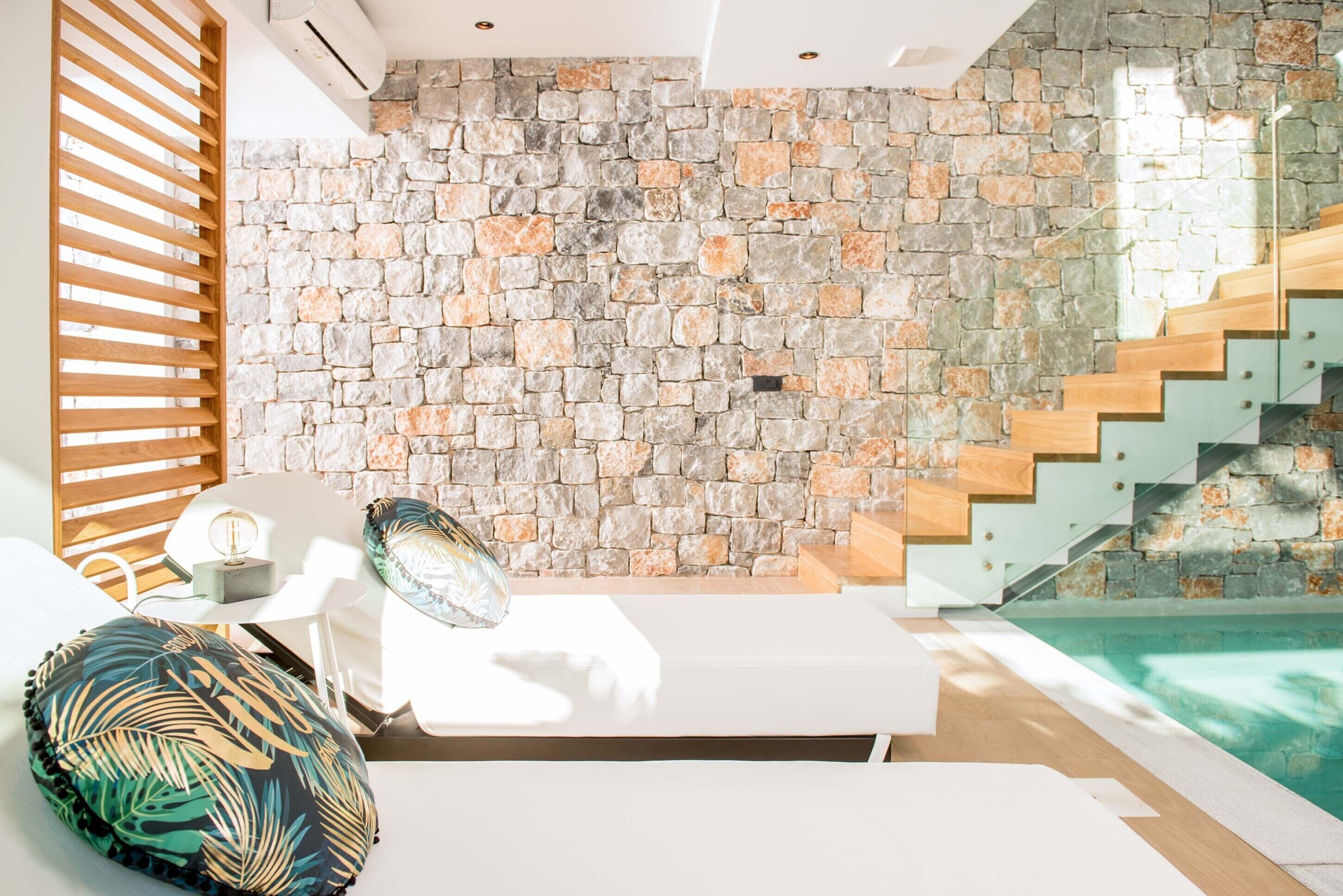 A modern room with a stone wall, a wooden staircase, and a pool.
