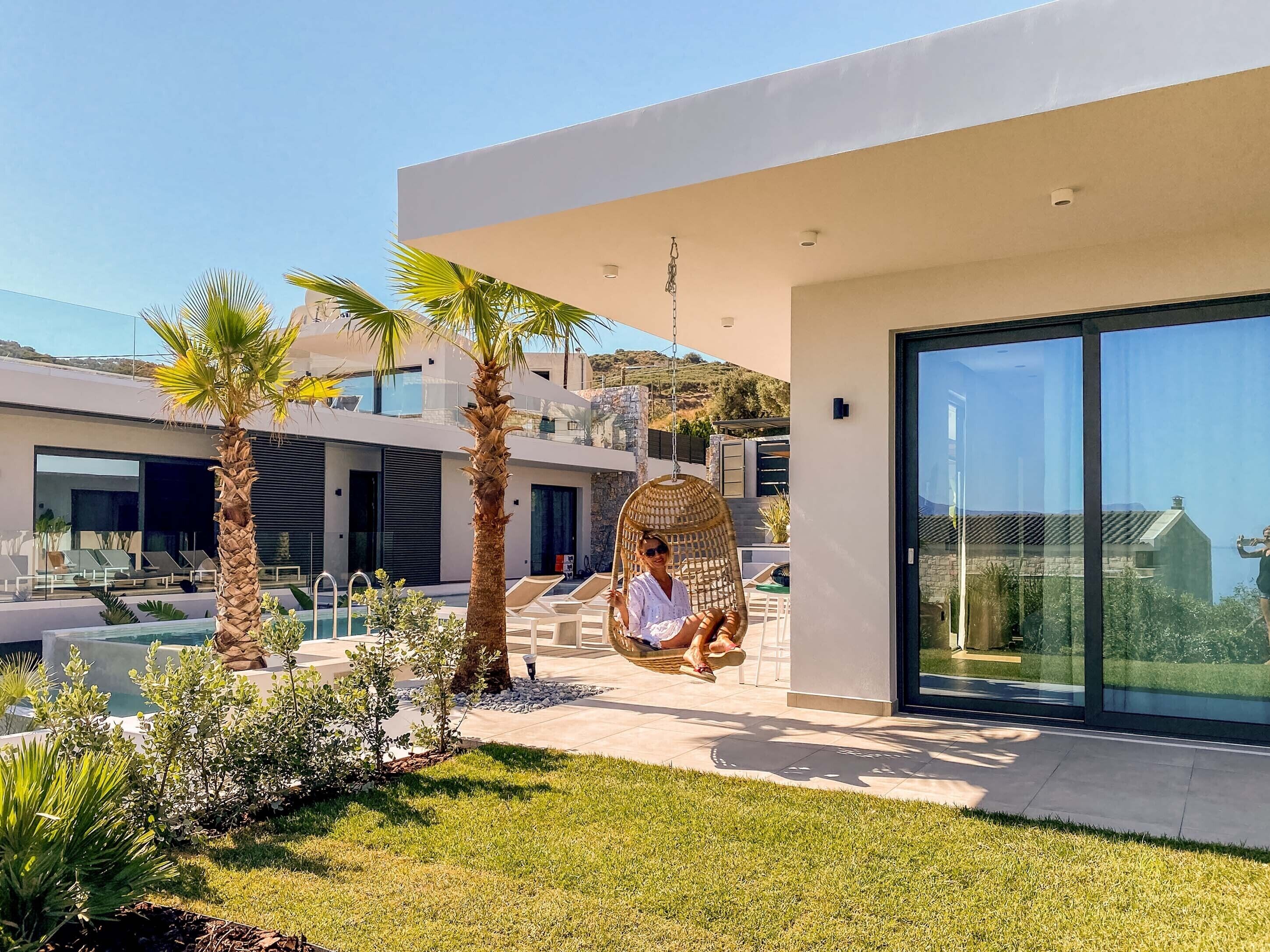 A modern outdoor area with a pool, palm trees, and a hanging chair.