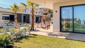 A modern outdoor area with a pool, palm trees, and a hanging chair. - Villa Lydia (Kissamos)