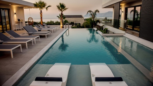 A pool area with lounge chairs, a table with chairs, and a view of the sea. - Villa Lydia (Kissamos)