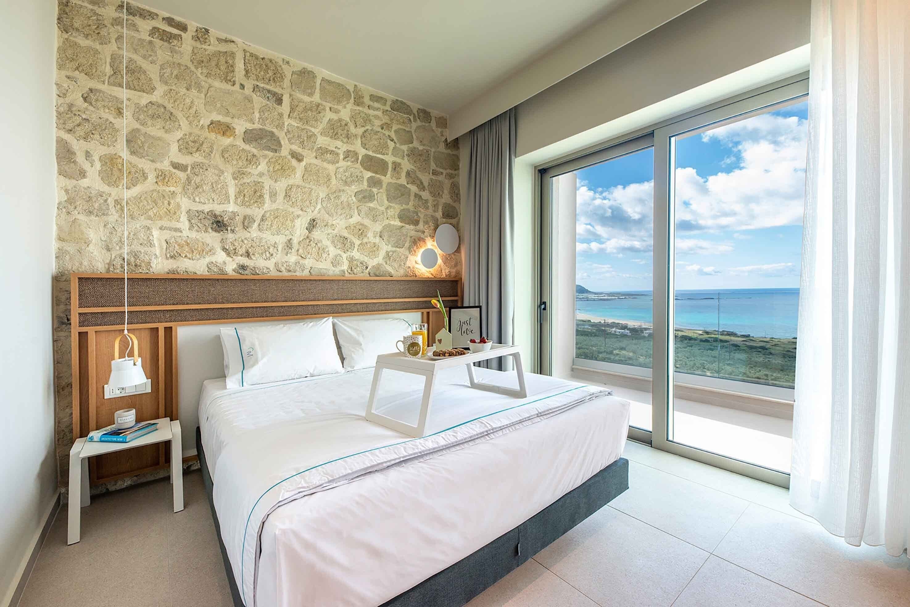 Una camera da letto con parete in pietra, un letto con vista, un comodino con lampada e un vassoio con oggetti.