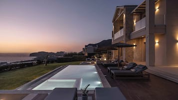 A modern pool area with lounge chairs and a view of the sea at dusk.