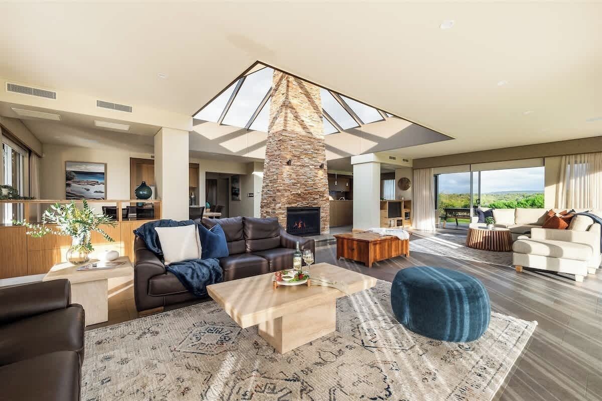 A spacious living room with a stone fireplace, a large skylight, and a view of the outdoors.
