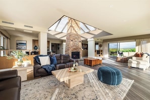 A spacious living room with a stone fireplace, a large skylight, and a view of the outdoors.