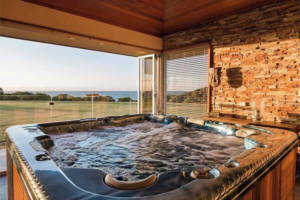 A hot tub with a view of a grassy field and a building in the distance.
