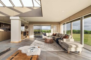 A spacious living room with a large window, a sofa set, a coffee table, and a wooden floor.