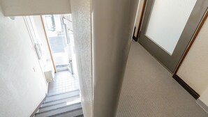 A narrow hallway with a carpeted floor, a door with a frosted glass panel, and a visible vent on the wall. - ILIMA Higashi Nakano (Tokyo)