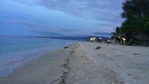 A beach with a sandy shore, a few buildings in the distance, and a body of water. - Nelly Bungalows (Gili Air)