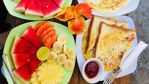 A table with plates of fruit, a cup of coffee, a plate of pancakes, and a sandwich. - Nelly Bungalows (Gili Air)