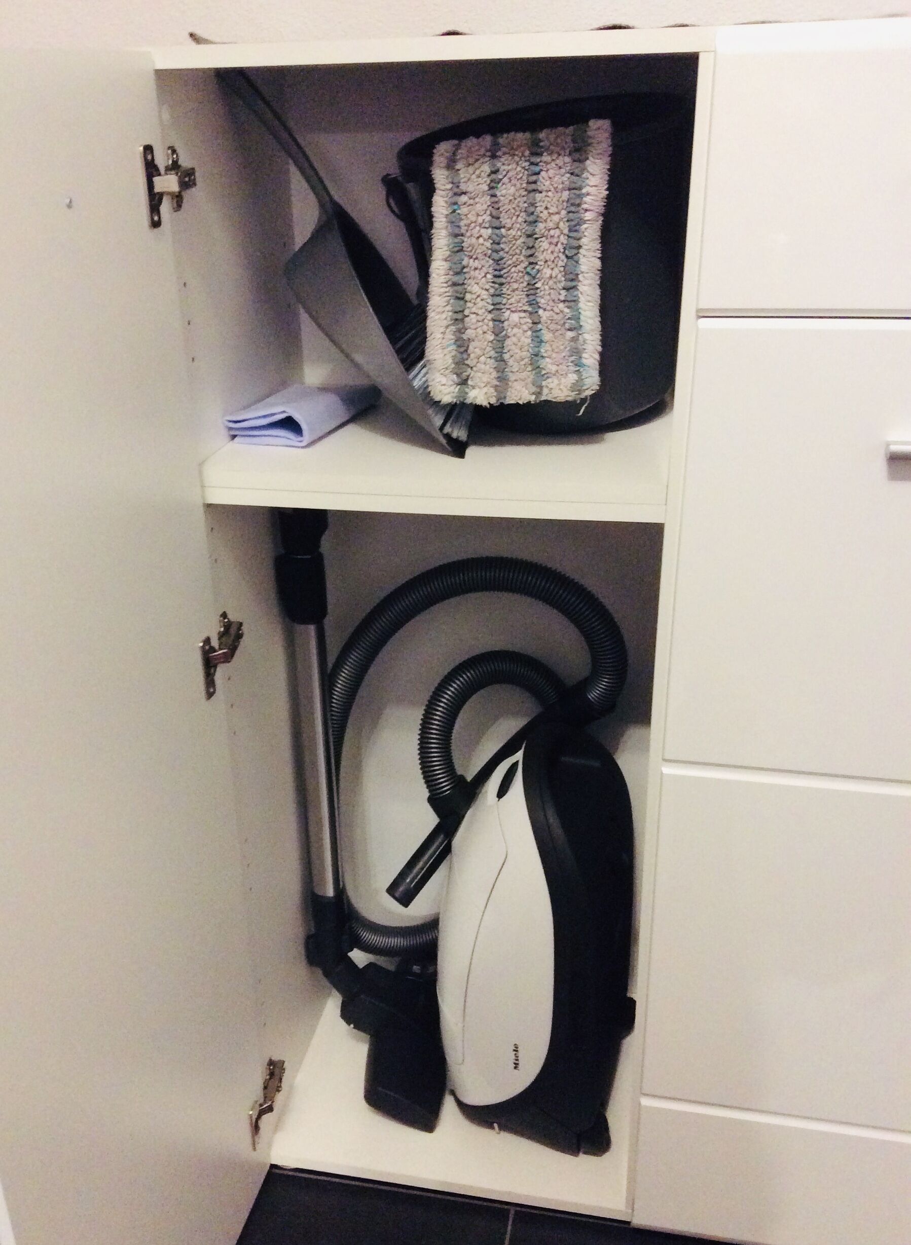 Ein Stauraumschrank mit Staubsauger und einem gemusterten Beutel darauf.