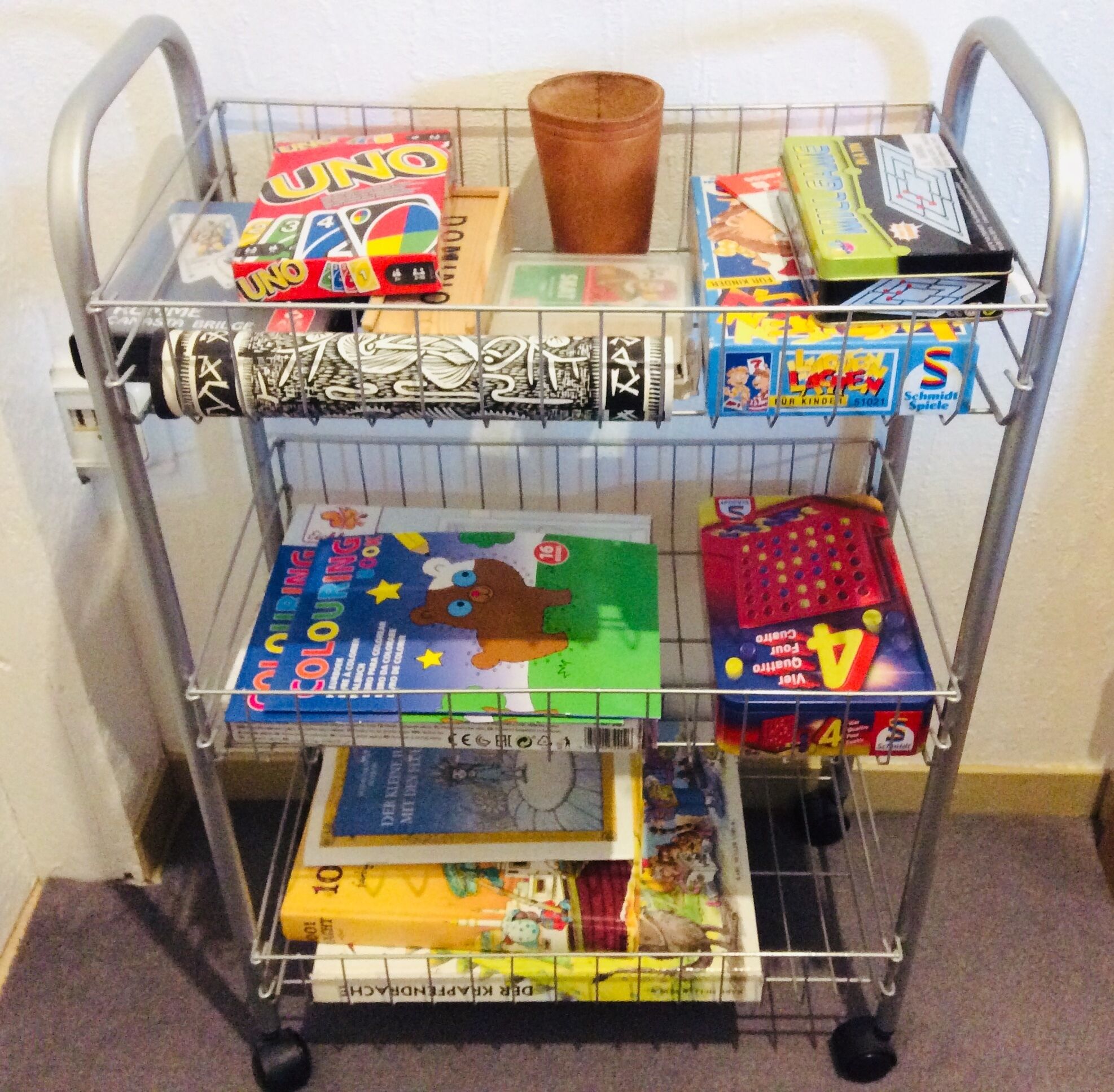 Un carrito metálico con diversos juegos y libros infantiles.