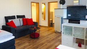 A living room with a sofa, a coffee table, and a TV. There is a kitchen area with a stove and cabinets. - Vacation apartment "Fernblick " (ZWEIBRÜCKEN)