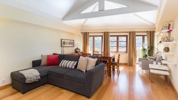 Uma sala de estar moderna com um sofá seccional, piso de madeira, uma área de jantar com mesa e cadeiras, e um claraboia.
