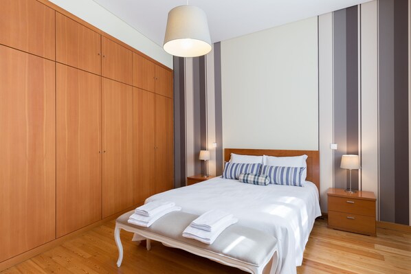 A neatly arranged bedroom with a wooden wardrobe, a bed with white linens, and two bedside tables with lamps. - Apartment - OPO 52 (Porto)