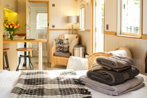 A hotel room with a bed, a chair, a table with a vase of flowers, and a window. - a beautiful rural shepherd hut with hot tub ! (Rushford)