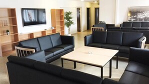 A modern living room with black sofas, a coffee table, and a TV mounted on the wall. There are wooden shelves and a potted plant. - Danhostel Thyborøn (Thyborøn)
