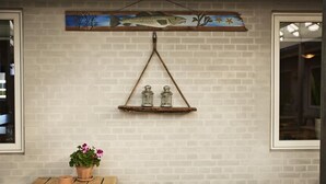 A rustic interior with a brick wall, a wooden shelf with two glass jars, a potted plant, and a framed fish painting. - Danhostel Thyborøn (Thyborøn)