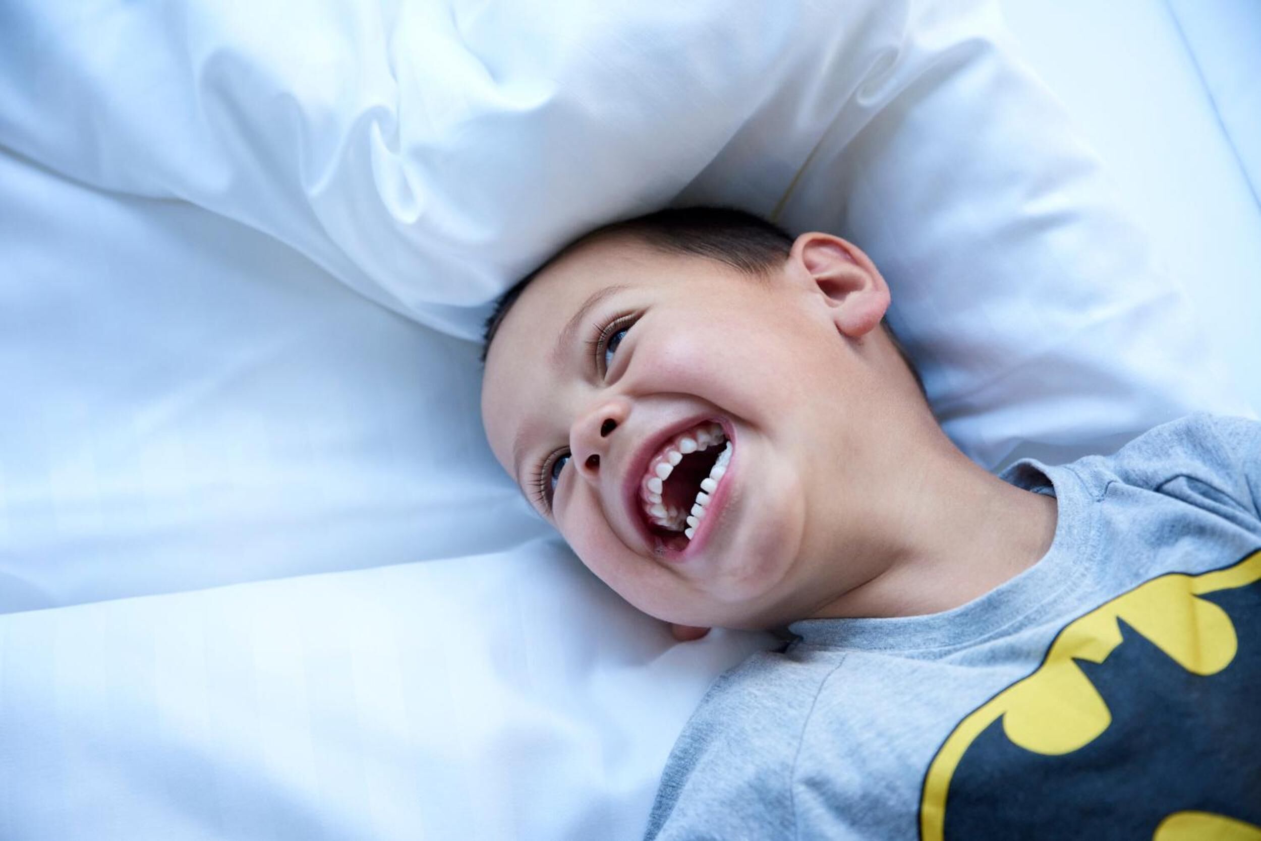 A child lying on a bed with white bedding.