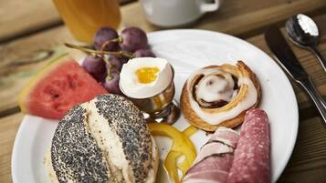 Un plato con una variedad de alimentos, incluyendo una rebanada de sandía, uvas, un huevo duro, un rollo de semillas de amapola, un pastel con crema y salami en rodajas.