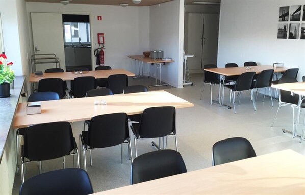 A conference room with multiple tables and chairs, a kitchenette in the background, and a fire extinguisher on the wall.