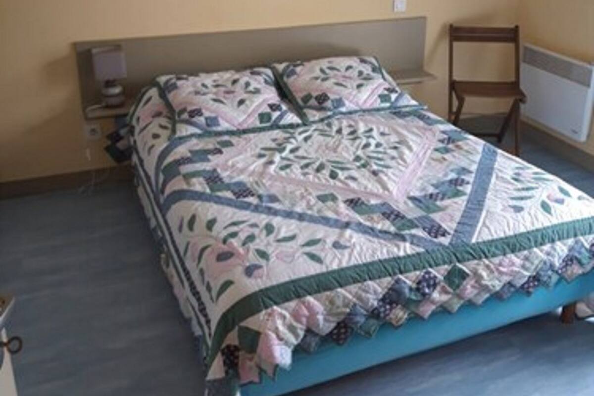 A bedroom with a bed, a nightstand, a chair, and a wall-mounted light fixture.