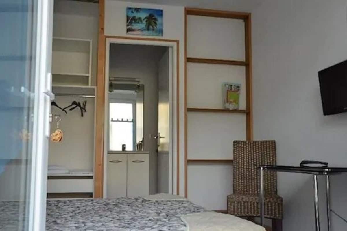 A bedroom with a bed, a wardrobe, a chair, and a TV on the wall.