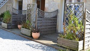 Un edificio in pietra con un patio di legno, piante in vaso e un cancello in metallo.