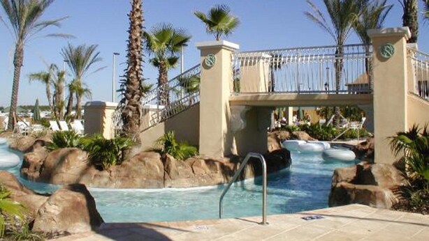 A pool area with a bridge, palm trees, and lounge chairs. - EPIC VALUE! Disney Retreat! Peter Pan! Resort! (Davenport)