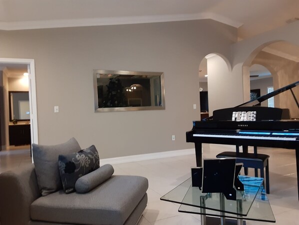 Uma sala de estar ampla com um piano de cauda, uma mesa de centro de vidro e um sofá moderno.