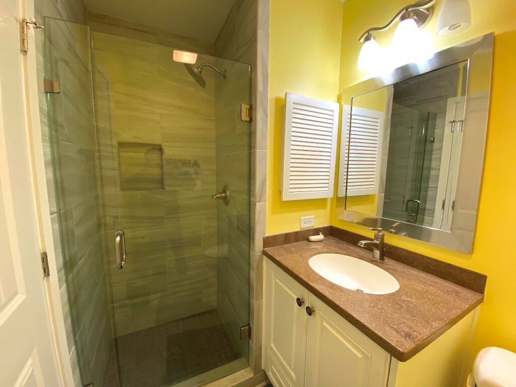 Un baño con ducha de vidrio, un lavamanos blanco y un espejo encima.