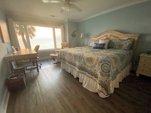 A bedroom with a large bed, a desk, and a chair, with a view of the ocean through a large window. - Ocean Views From Your Own Balcony, 3 Bedroom Villa, 634 New Haven Court (Fripp Island)