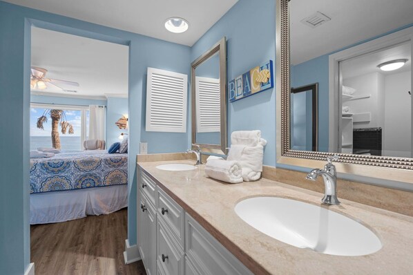A bathroom with a double sink, a large mirror, and a view of the sea through a window.