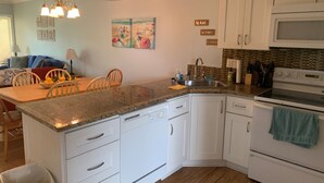 A kitchen with white cabinets, a granite countertop, a sink, a stove, and a dining area with a table and chairs.