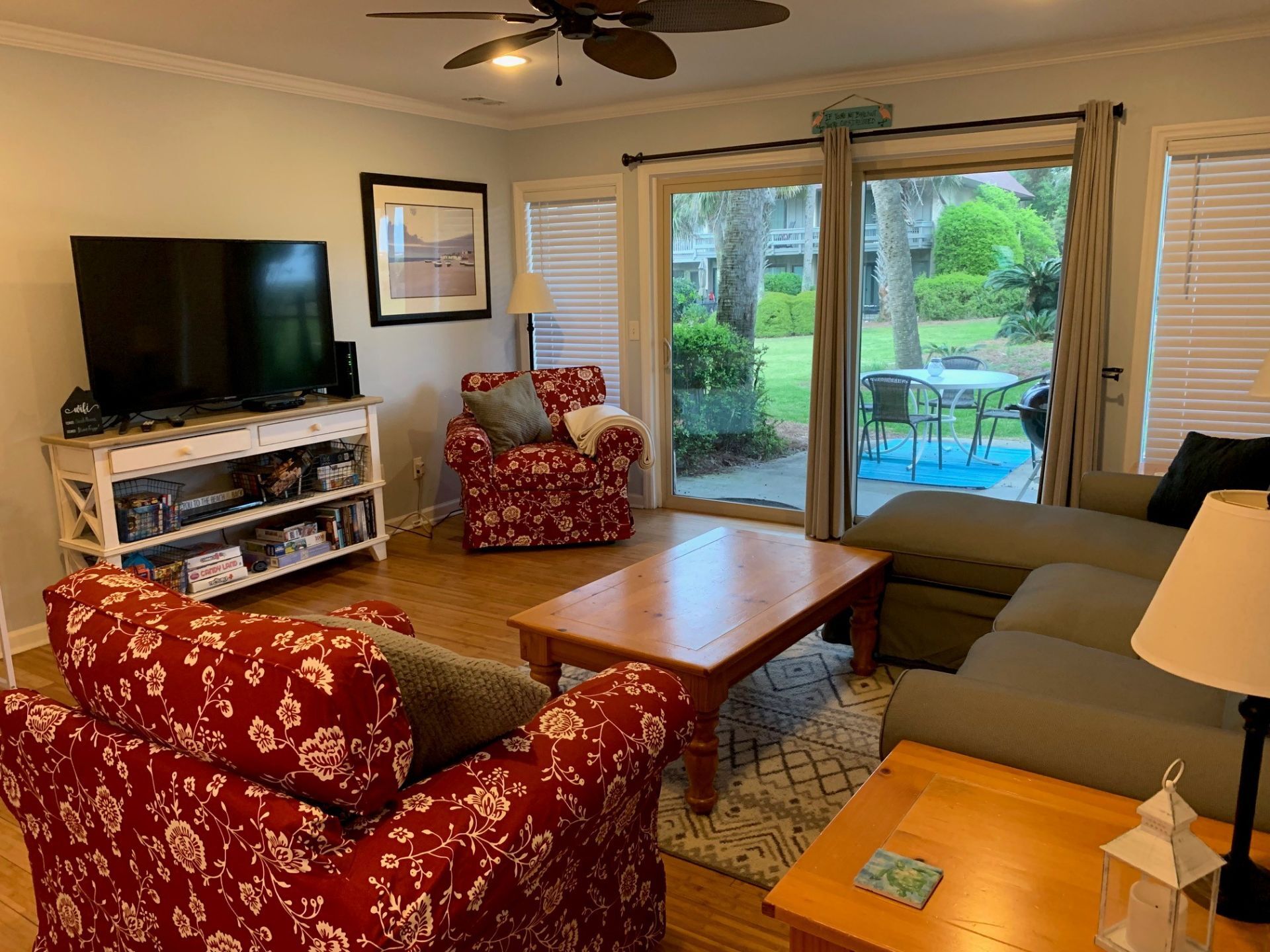 A living room with a TV, a sofa, a red floral armchair, a wooden coffee table, and a bookshelf.