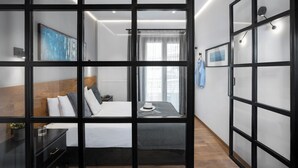 Ein modernes Hotelzimmer mit einem großen Bett, einem Nachttisch, einem Kleiderschrank und Blick durch eine Glastrennwand.