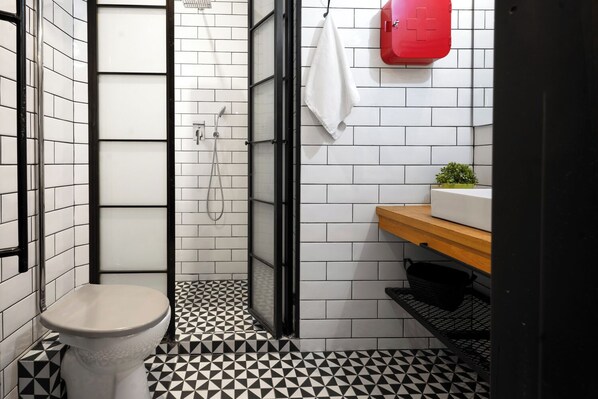 A bathroom with a toilet, shower, and sink with a red cabinet.