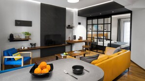 Ein modernes Wohnzimmer mit einer Couch, einem Esstisch mit Obst, einem Couchtisch und einem Fernseher.