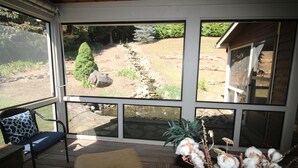 A covered outdoor seating area with a view of a landscaped garden, including a pond and a wooden deck. - Luxury Mountain Cabin w/ Hot Tub 75 Private Acres, & Near New River (Jefferson)