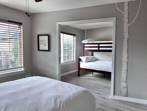 A bedroom with a bunk bed, a large window with blinds, a framed picture on the wall, and a tree mural on the wall.