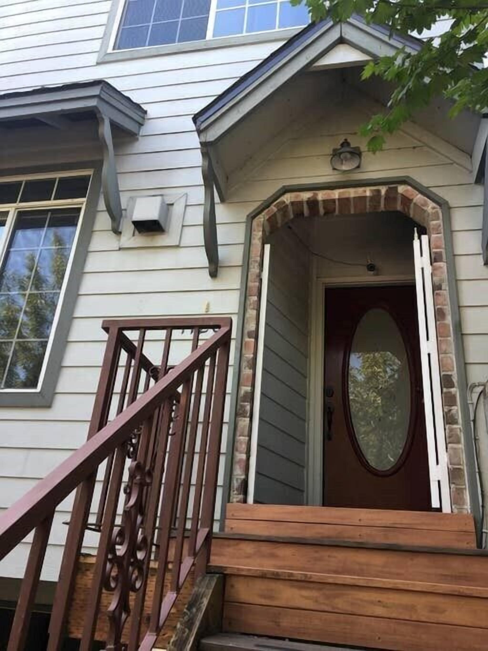 A house with a front porch, a wooden staircase, and a brick archway.