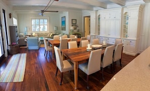 Un grand espace à manger avec une table et des chaises en bois, une cuisine dotée de meubles blancs et un salon avec un canapé et une table basse.
