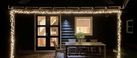 A covered outdoor area with a table and chairs, a potted plant, and a window with blinds.