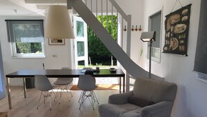 A modern living room with a staircase, a dining area, and a large window with a view of greenery.