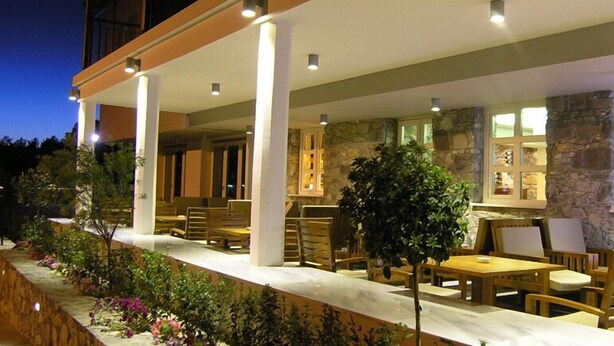 Un patio al aire libre con mesas y sillas de madera, paredes de piedra y un ambiente bien iluminado.
