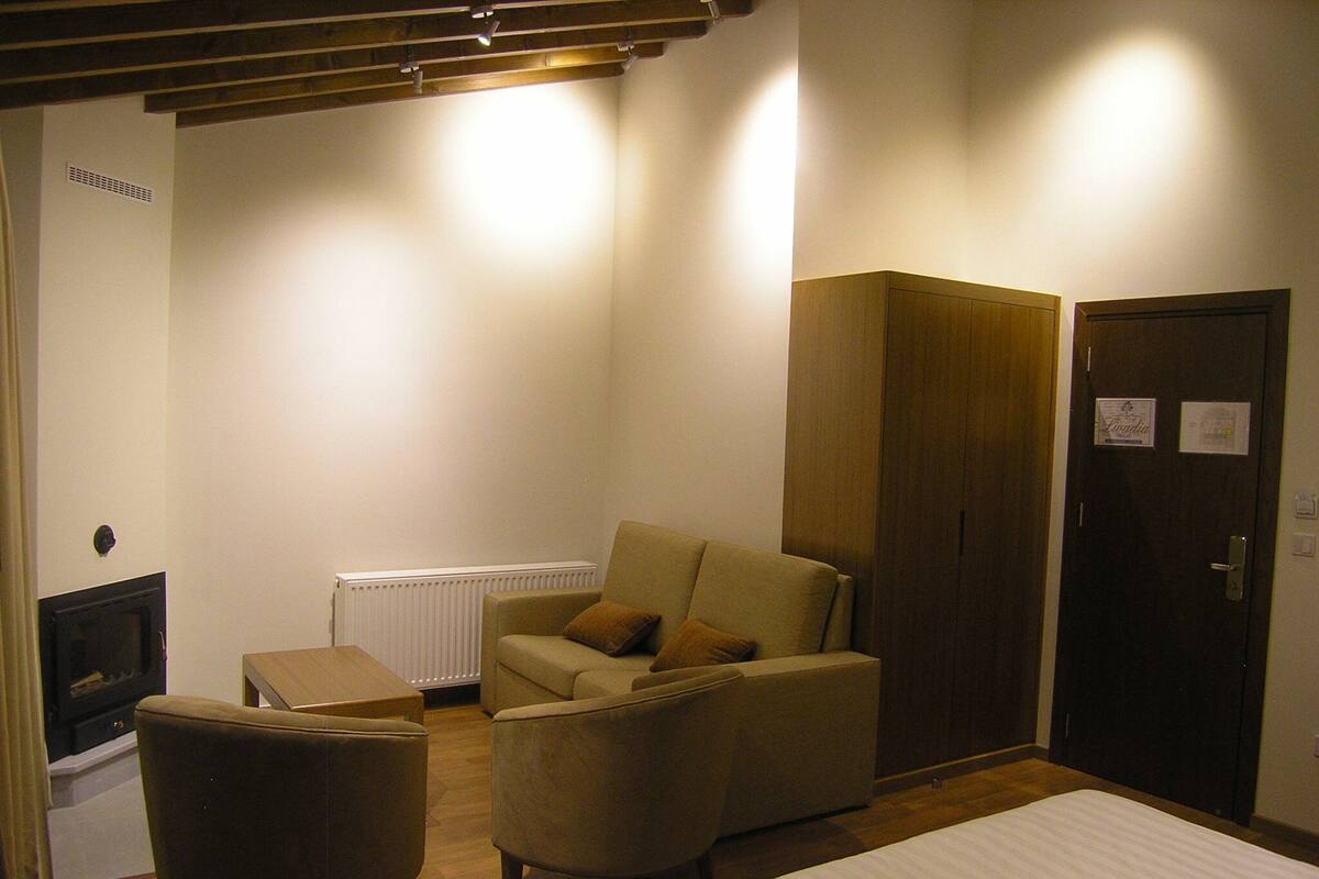 Een hotelkamer met een bed, twee fauteuils, een houten garderobe, een radiator en een deur met een bordje.