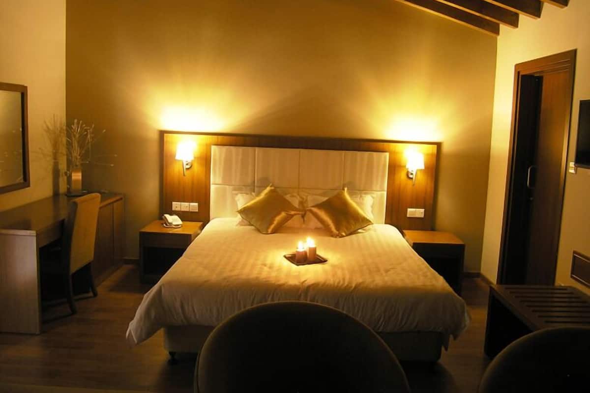 Een hotelkamer met een groot bed, twee nachtkastjes met lampen, een stoel en een klein tafeltje met een vaas.